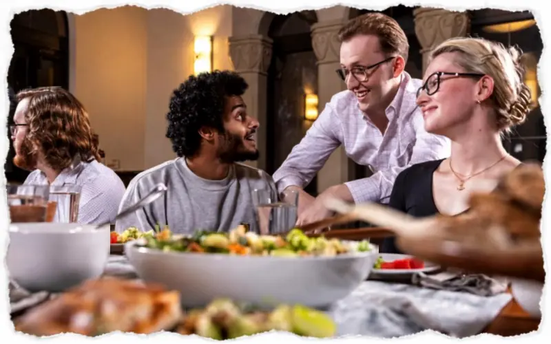 Hands passing a shared bowl of pasta at a full table